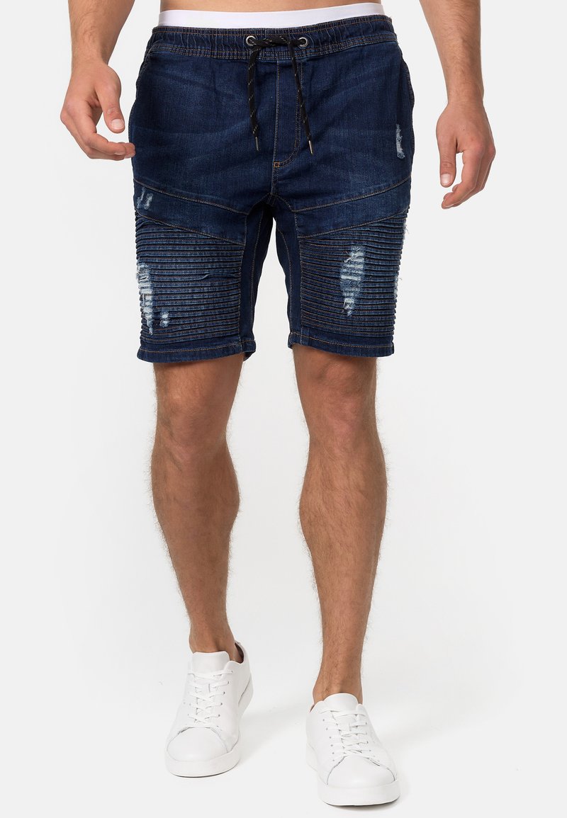 Shorts en denim bleu foncé avec une texture côtelée sur les côtés, présentant des accents usés et une taille élastique avec cordon de serrage.