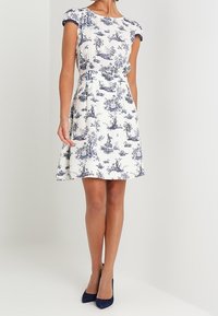 Blommig klänning i vitt och marinblått, med korta ärmar, figursydd midja, utsvängd kjol och en mjuk bomullstextur.