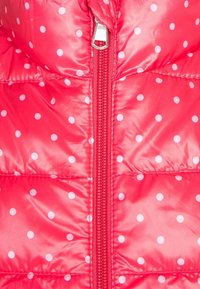 Roter gepolsterter Stoff mit weißen Punkten, der einen zentralen rosa Reißverschluss und gesteppte Nähte aufweist.