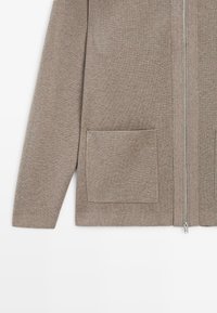 Brauner Reißverschluss-Cardigan aus Strickstoff. Mit langen Ärmeln, geradem Schnitt und zwei Vorderentaschen. Glatte Textur und minimalistisches Design.