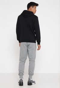 Sweat à capuche noir avec cordon de serrage, associé à un pantalon de jogging gris clair avec des poignets élastiques. La tenue est complétée par des chaussures de sport sombres.