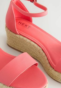 Korall színű wedge szandálok texturált műbőr pántokkal, nyitott orral és fonott jutebéléssel. Állítható boka pánt tartozik hozzá.