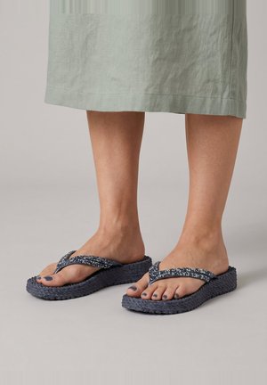 Voeten met donkerblauwe slippers met dikke zolen en gevlekte bandjes, gecombineerd met een lichtgroene rok die boven de enkels valt.