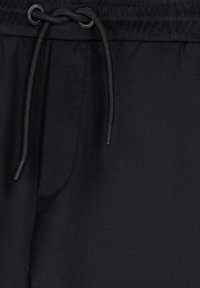 Schwarze Jogginghose mit elastischem Bund und Kordelzug. Weicher Stoff, seitliche Tasche sichtbar, glatte Textur ohne sichtbare Muster oder Akzente.