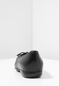 Svart lädersko med platt sula och rund tå, slät yta, minimalistisk design och en liten rosett ovanpå.