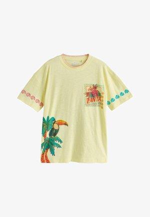 Żółta koszulka z krótkim rękawem z tropikalnymi wzorami, w tym tukaniem na palmie i kwiatową naszywką z napisem "TANTA."