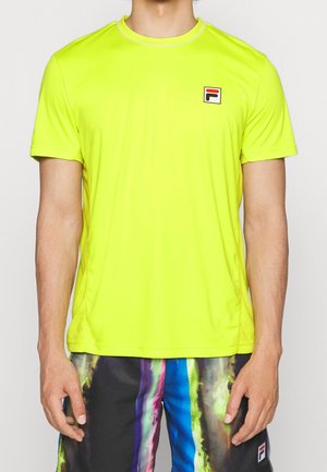 Mand iført en klar gul kortærmet sportstrøje og flerfarvede stribede atletikshorts, der står mod en hvid baggrund.