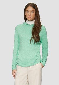 Hellgrüner Kapuzenpullover aus strukturiertem Stoff mit einer Kängurutasche und langen Ärmeln. Kombiniert mit beigen Hosen.