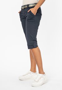 Marineblauwe knielange cargoshorts met zakken en opgerolde manchetten, gemaakt van lichtgewicht katoen. Gecombineerd met witte sneakers en een eenvoudige riem.