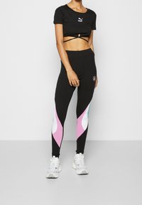 Svart kortärmad t-shirt med ribbad textur och PUMA-logotyp, i kombination med svarta leggings med rosa, vita och turkosa vågmönster. Vita sneakers.