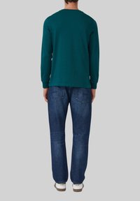 Langärmliges türkisfarbenes Shirt mit rundem Halsauschnitt, kombiniert mit blauen Jeans und weißen Sneakers. Das Outfit hat eine legere, entspannte Passform.