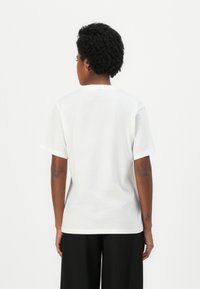 Witte t-shirt met korte mouwen en een ronde hals, gemaakt van zachte katoen, heeft een ontspannen pasvorm en een label aan de achterkant van de hals, met een effen textuur.