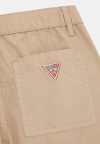 Khaki színű rövidnadrág, hátsó zsebbel, piros és fehér háromszög alakú "GUESS" logóval. Könnyű anyagból készült, sima tapintással.