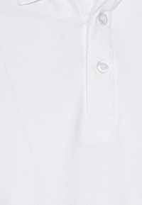 Hvit polo skjorte laget av teksturert bomullsstoff, med en tre-knaps placket og myk krage. Ren, enkel design uten mønstre.