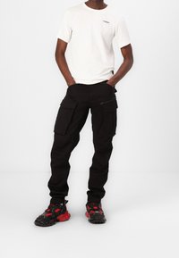 Czarne spodnie cargo z wieloma kieszeniami, w połączeniu z gładką białą koszulką. Obuwie charakteryzuje się czarnymi i czerwonymi detalami oraz masywnym designem.