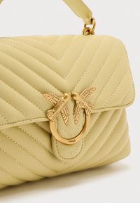 Κίτρινη τσάντα χειρός από δερμάτινο υλικό με ανάγλυφο σχέδιο ζιγκ-ζαγκ, χρυσούς μεταλλικούς κόμπους σε σχήμα πουλιού και δομημένο σχήμα.