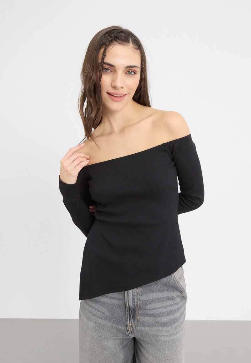 Schwarzes, schulterfreies Langarmoberteil aus geripptem Material. Enganliegendes Design mit abgerundetem Saum, kombiniert mit hellgrauen Jeans.