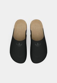 Melnas atvērtā aizmugurē slides no gludas materiāla, ar brūnu pēdu un smalku melnu logo detaļu augšējā daļā.