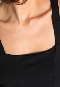 Svart ärmlös plagg med fyrkantig halsringning. Tyget verkar mjukt med en jämn textur. Har en ren, minimalistisk design.