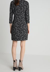 Abito a pois in bianco e nero con maniche a tre quarti, lunghezza al ginocchio, abbinato a stivaletti grigi chiari con tacco a blocco.