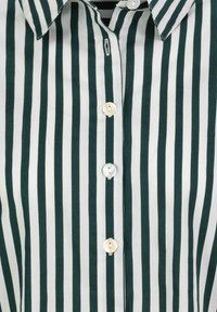 Green and white striped button-up shirt with a classic collar. Features six round buttons along the front, textured fabric, and vertical stripes.