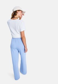 Camiseta corta de manga corta blanca combinada con pantalones anchos de talle alto en azul claro. Una gorra beige completa el atuendo.