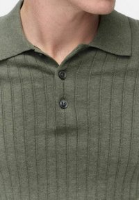 Knitpolo i olivgrön, med vertikal ribbning, klassisk krage och två mörka knappar på placket. Strukturerad yta.