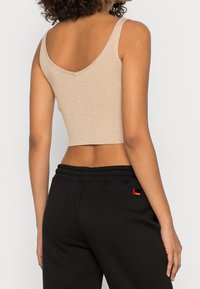 Beżowy prążkowany top z dekoltem w serek z tyłu, połączony z czarnymi dresami z czerwonym akcentem logo na talii. Prosty i dopasowany fason.