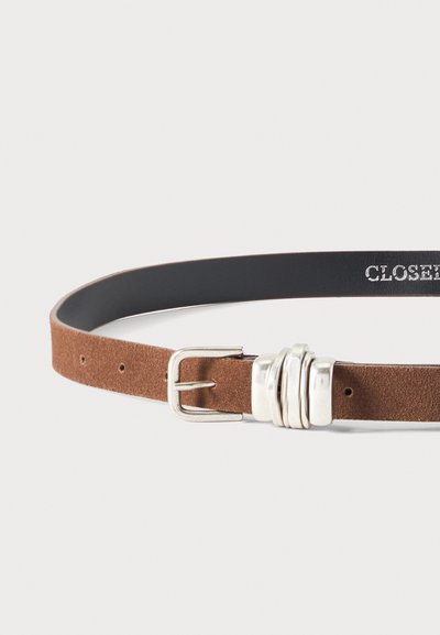 Ceinture en daim marron avec boucle argentée et trois passants argentés sur fond blanc.