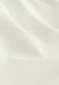 Tissu blanc avec une texture lisse et subtile, un motif côtelé diagonal, drapé et légèrement froissé.