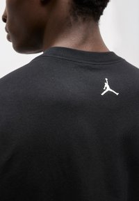 Άτομο που φοράει μαύρο πουκάμισο με μικρό λευκό λογότυπο καλαθοσφαιριστή κοντά στο λαιμό στην πίσω πλευρά.