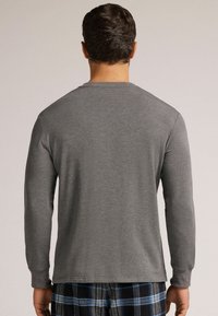 Grauem Langarmshirt aus weichem Stoff, mit einem einfachen Rundhalsausschnitt und schmaler Passform sowie gerippten Bündchen, getragen mit karierten Schlafanzughosen.