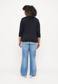 Svart topp med trekvarts ermer kombinert med lyseblå vide jeans; stoffet ser mykt ut, med en jevn tekstur. Fottøyet er hvite sneakers.