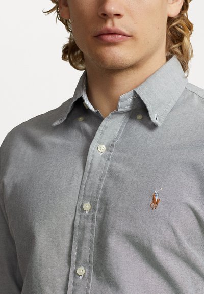 Chemise gris à motifs texturés, dotée d'un petit logo brodé sur la poitrine et d'accents de boutons blancs. Design décontracté.
