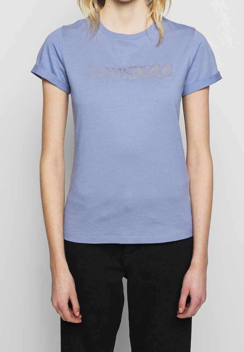 T-shirt en coton bleu clair avec un col rond, des manches courtes retroussées et un logo imprimé plus foncé sur la poitrine.