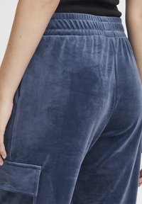 Námornícke modré velúrové tepláky s uvoľneným strihom, elastickým pásom a detailom bočného vrecka. Mäkka textúra s hladkým povrchom.