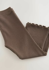 Brūnas ribotas leggingas ar mīkstu tekstūru un viļņotu apakšmalu. Materiāls izskatās elastīgs un ērts ikdienas nēsāšanai.