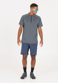 Grå kortärmad sporttröja med dragkedja i kragen, tillsammans med mörkblå shorts. Enfärgade skor och svarta ankelsockor fulländar outfiten.