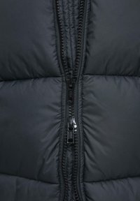 Zwart pufferjackett texture met een zichtbare ritsdetail. De stof lijkt glad en geïsoleerd, met gestikte secties.