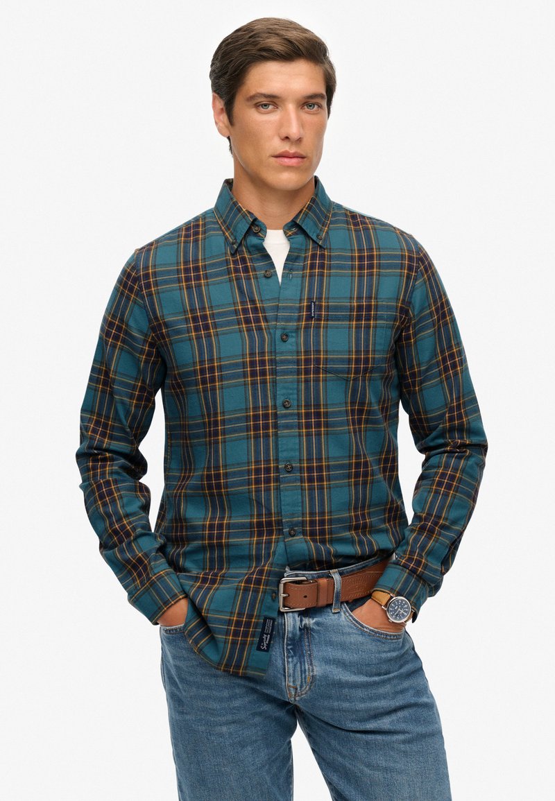 Camisa de cuadros de manga larga en teal con acentos marrones y amarillos. Presenta un cuello con botones, un bolsillo en el pecho y una tela suave y texturizada.
