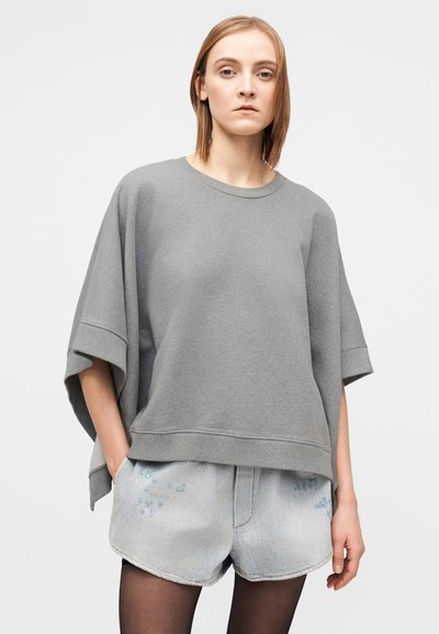 Siva prevelika majica iz mehke tkanine z okrolim izrezom in rokavi do komolca. Kombinirana s svetlo denim kratkimi hlačami.