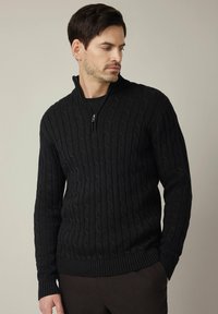 Czarny sweter w warkocze z wysokim kołnierzem i zamkiem na pół długości. Wykonany z fakturowanego dzianinowego materiału, z prążkowanymi mankietami i dołem.