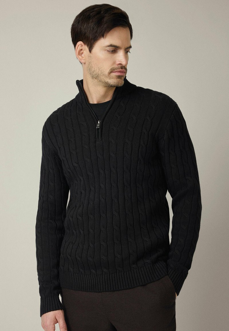 Czarny sweter w warkocze z wysokim kołnierzem i zamkiem na pół długości. Wykonany z fakturowanego dzianinowego materiału, z prążkowanymi mankietami i dołem.