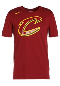 Camiseta de algodón roja con un gran logo "C" en amarillo y negro, brillante en la parte frontal. Diseño de manga corta y cuello redondo.