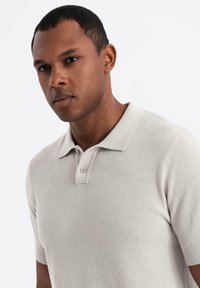 Kortærmet, lysegrå polo-shirt med et tekstureret strikkemønster og en to-knap placket. Har en klassisk krave og tætsiddende design.