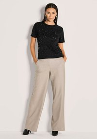 Zwarte T-shirt met korte mouwen en verspreide metallic versieringen, gecombineerd met lichtbeige wijde broek en zwarte hakken.
