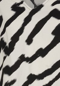 Top bianco e nero con motivo a zigzag, realizzato in un tessuto morbido con scollatura a V e una consistenza leggera.