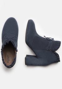 Botas de tobillo azul marino hechas de suave ante, con un borde superior con volantes, diseño de cordones y un tacón grueso para mayor estabilidad.