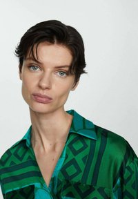 Cămașă verde cu un model geometric, textură de saten, mâneci scurte și guler.