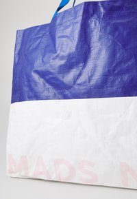 Blå og hvit vevd totebag med en teksturert overflate, med blå håndtak og rosa tekst på den nederste hvite delen.